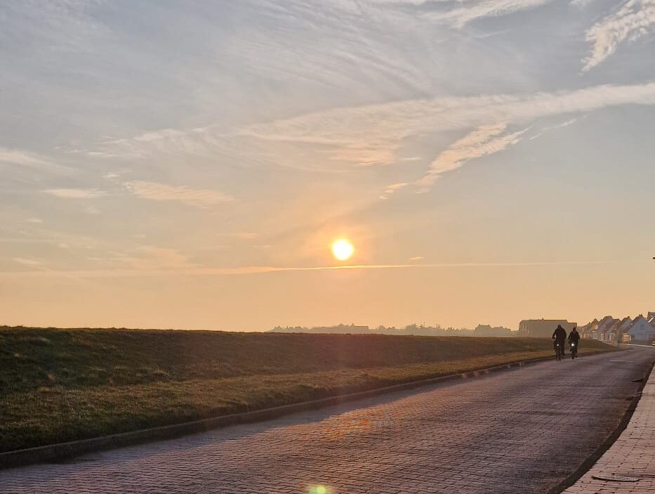 Sonnenuntergang hinter dem Deich, am rechten Rand zwei Radfahrer