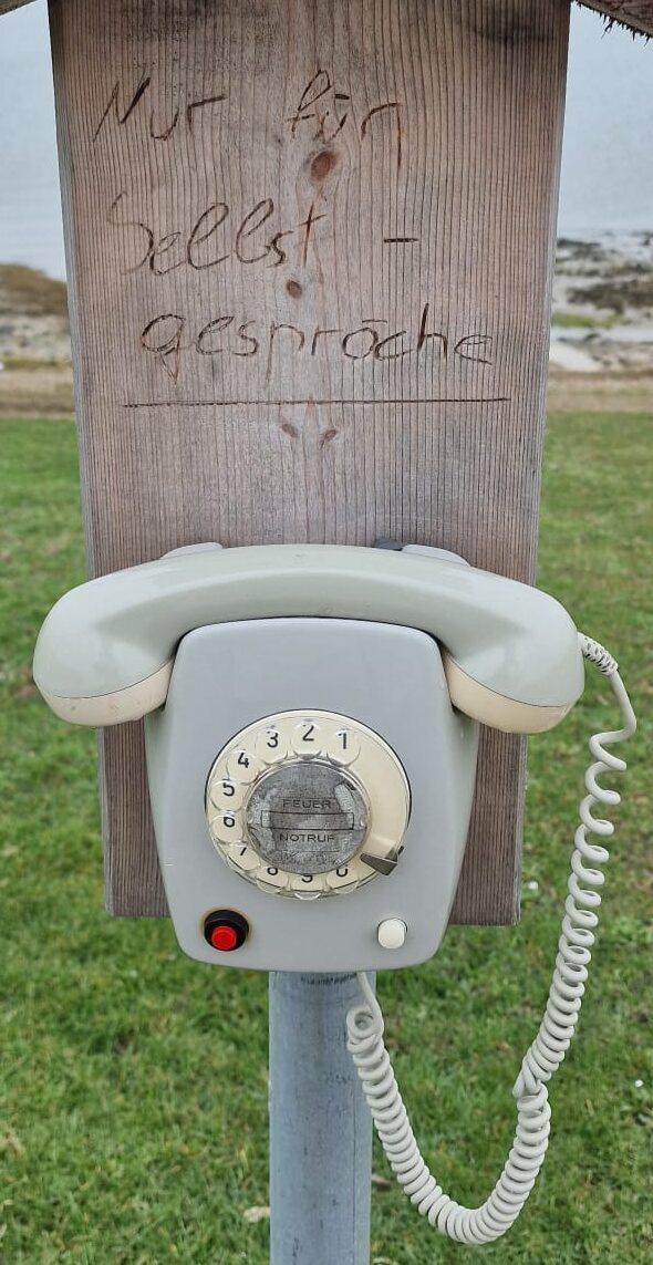 altes Wählscheibentelefon ohne Funktion auf einem Holzbrett mit der Aufschrift: nur für Selbstgespräche